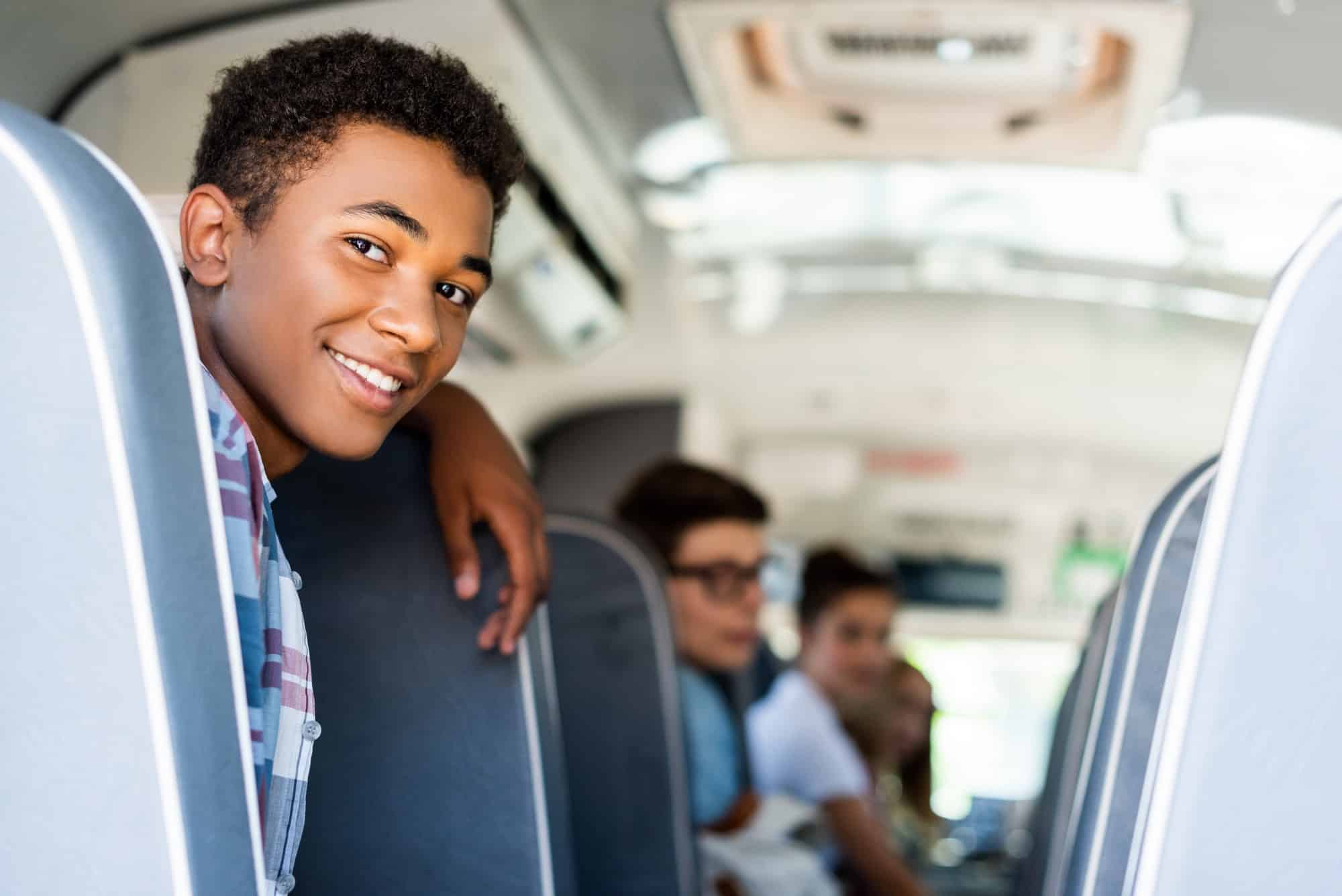 teen students sitting at school bus and looking back at camera