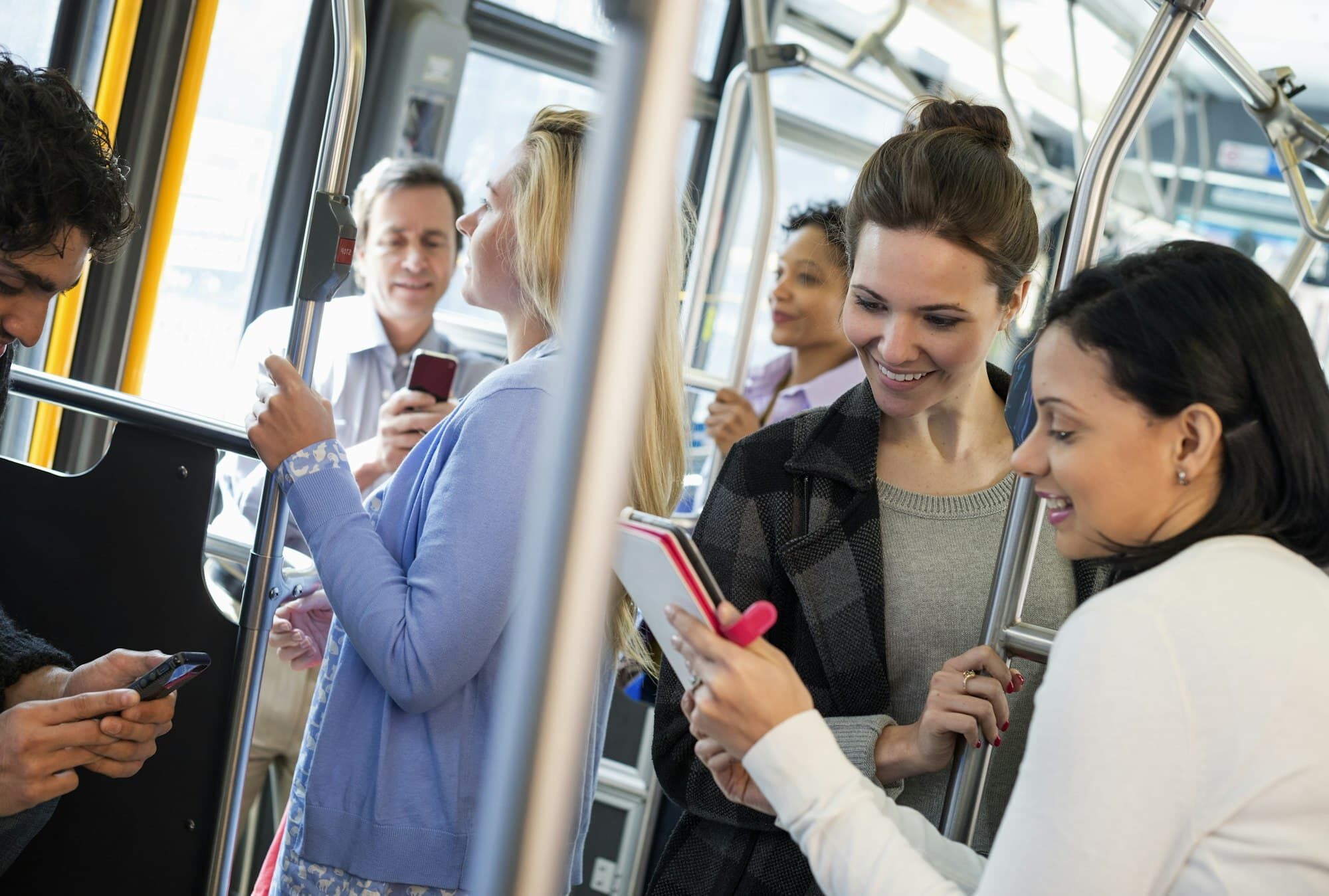 Men and women on a city bus. Public transport. Two women looking at a handheld digital tablet.